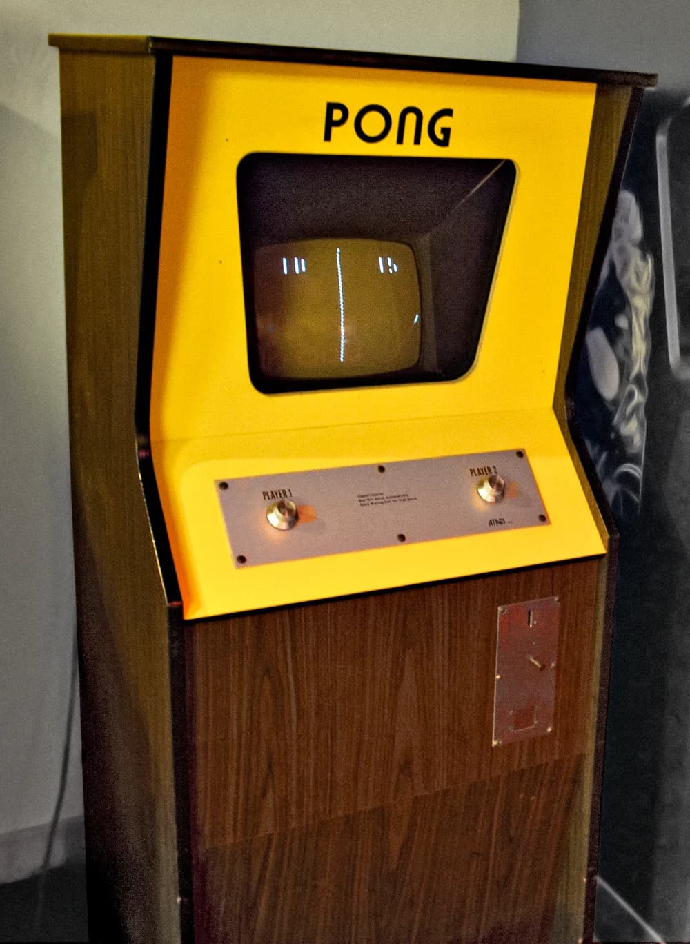 Borne d'arcade Pong d'origine (Atari, 1972) : caisson en bois, panneau jaune, écran noir et blanc affichant le duel de raquettes et deux molettes de contrôle