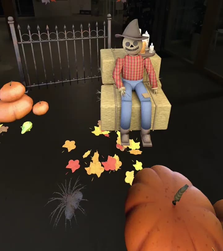 Vue dans le casque : un épouvantail assis sur une botte de foin, une grille, des citrouilles et des feuilles mortes en 3D posés dans une vraie salle, en réalité mixte
