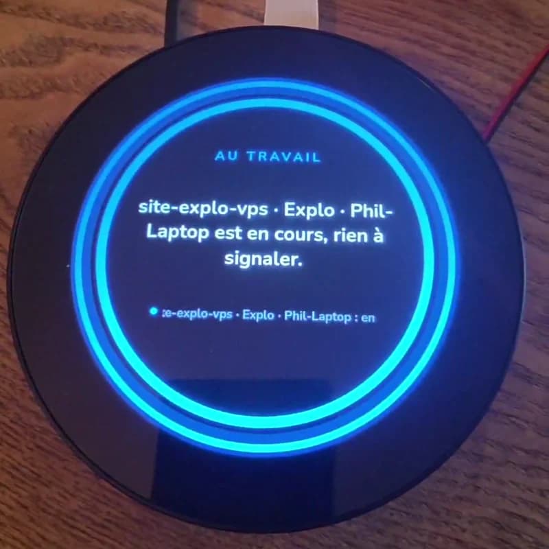 L'écran rond de la Vigie pendant qu'un agent travaille : double anneau bleu lumineux, mention « Au travail » et la phrase « site-explo-vps · Explo · Phil-Laptop est en cours, rien à signaler »