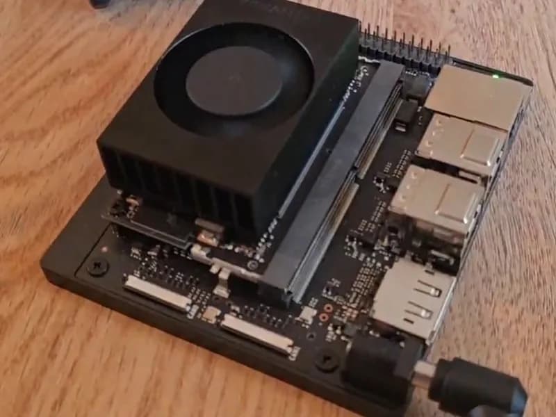 La carte NVIDIA Jetson Orin Nano posée sur un bureau en bois, avec son radiateur et son ventilateur noirs, ses ports USB et Ethernet, et le câble d'alimentation branché